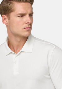 Polo bianco con collo a camicia,patta con tre bottoni e tessuto texture, che mette in risalto una silhouette aderente.