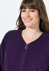 Fialová fleecová bunda na zip s kulatým výstřihem, texturovaná látka a stříbrný zip vpředu. Měkký a ležérní design.