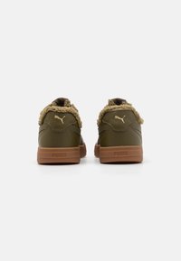 Par de zapatillas Puma de color verde oliva con suelas marrones y forro de borrego beige, vistas desde la parte trasera sobre un fondo blanco.