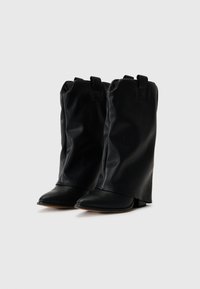 Botas de cuero negro hasta el tobillo con un diseño arrugado, puntas puntiagudas y pequeños tacones de bloque. Presenta dos detalles de tira en la parte superior.