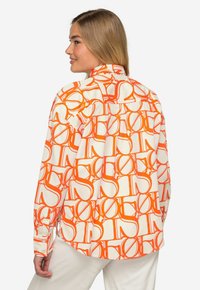 Camicia button-up con base bianca e motivo grafico arancione. Presenta un colletto classico, maniche lunghe e un orlo curvo.