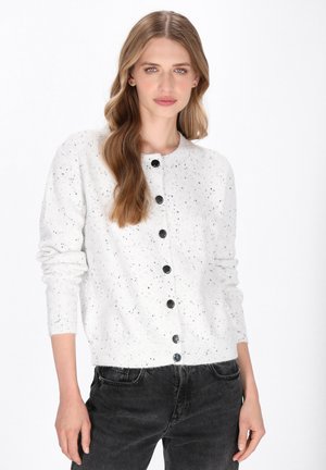 Cardigan bianco a maglia con macchie nere, scollatura rotonda e bottoni neri lungo il davanti. Maniche lunghe e polsini a coste.