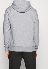 Sweat-shirt gris à capuche, avec une texture lisse, des poignets et un ourlet côtelés. Le design est simple, sans motifs ni accents.