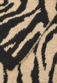 Tessuto lavorato a maglia con motivo a strisce zebrato nero e beige, che mostra il filato strutturato e un bordo a coste sul polsino.