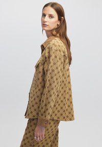 Braun gemusterte Jacke mit Wildlederkragen, im boxy Schnitt und großen Vordertaschen. Glatte Textur mit Knopfdetails.