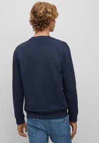 Felpa blu navy, colletto rotondo, maniche lunghe, polsini e orlo a costine, texture liscia, abbinata a jeans azzurri chiari. Design semplice, senza motivi visibili.