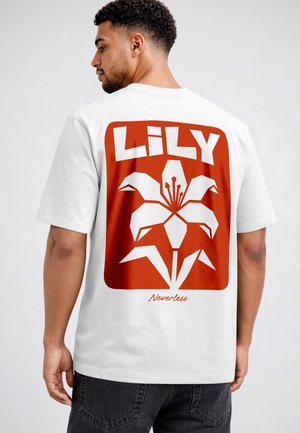 Mann mit dem Rücken zur Kamera, trägt weißes T-Shirt mit großem roten Motiv einer stilisierten Lilienblume und den Schriftzügen "LILY" und "Nevertheless" auf dem Rücken.
