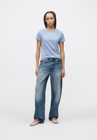 Light blue crew-neck t-shirt paired with high-waisted, faded blue wide-leg jeans. Model wears light-colored shoes, standing on a neutral background.