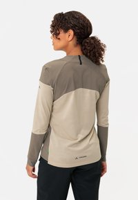 Chemise à manches longues en matériaux beige et gris, présentant un dos en maille, des manches raglan, et un branding subtil au niveau de l'ourlet.