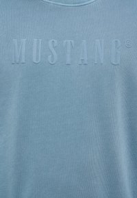 Sweatshirt bleu clair avec une texture côtelée et le logo en relief "MUSTANG®" sur la poitrine. Tissu doux avec un design classique à col rond.
