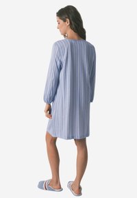 Abito blu a righe con vestibilità rilassata, maniche lunghe e scollatura arrotondata. Le ciabatte presentano un tessuto azzurro chiaro e dettagli a righe bianche.