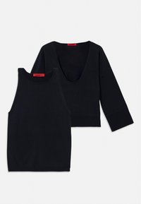 L'outfit nero a due pezzi include un top senza maniche e un top a maniche lunghe cropped, entrambi realizzati in un tessuto morbido e elasticizzato. Texture liscia.
