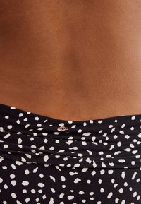 Svart tyg med ett vitt prickigt mönster, med samlad detaljering och en liten metallisk accent på baksidan. Mjuk textur.