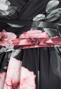 Tecido com estampado floral em preto, com flores rosa e brancas. Apresenta pregas e um acabamento texturizado com uma faixa decorativa.