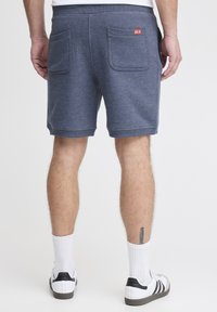 Blå atletiske shorts med tekstureret stof, elastisk talje og to baglommer. Rød logoetiket på den højre lomme.