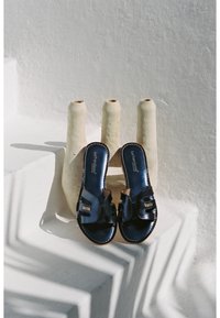 Sandali blu scuro con una finitura in pelle lucida, dotati di un design open-toe, cinturini regolabili e accenti dorati minimalisti.