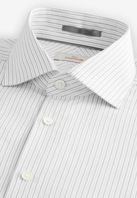 Chemise à rayures blanches avec une texture douce, dotée d'un col classique et de boutons vert clair. L'étiquette indique "NEXT SIGNATURE."