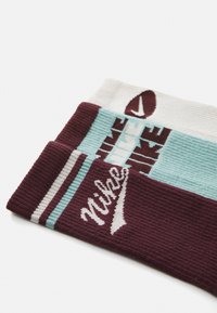Trzy pary skarpet Nike z teksturą w prążki. Kolory to bordowy, biały i morski, każda para ma wyraźne logo i paski.