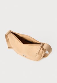 Beige stoffbæresekk med glidelås, justerbar stropp og en liten logo på forsiden. Glatt tekstur og enkel design.