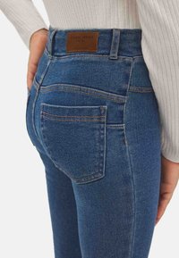 Jeans ajustados de denim azul oscuro con costuras naranjas contrastantes. Presenta un parche de marca de cuero y un diseño estándar de bolsillo trasero.