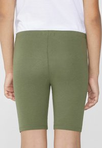 Zielone bawełniane szorty stretchowe o dopasowanym kroju, sięgające do połowy uda. Materiał jest gładki z lekkim połyskiem i elastycznym paskiem w talii.