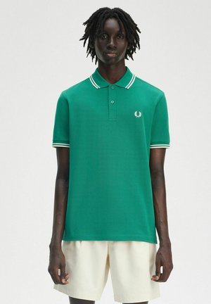 Grüne Poloshirt aus glattem Baumwollstoff, mit klassischem Kragen, Knopfleiste mit zwei Knöpfen und weißen Streifenakzenten am Kragen und an den Ärmeln.
