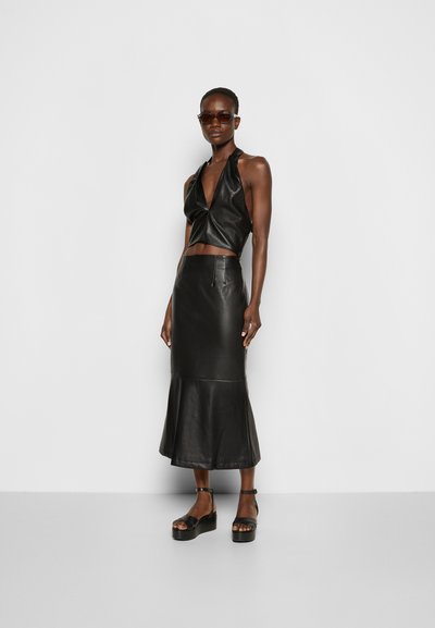 Top de halter de couro preto e saia sereia, apresentando uma textura suave e um silhueta ajustada. Usada com sandálias de plataforma pretas.