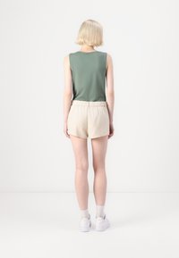Zelený top bez rukávov s okrúhlym výstrihom, skombinovaný s béžovými ľanovými šortkami. Model stojí chrbtom k fotoaparátu a má na sebe biele tenisky.