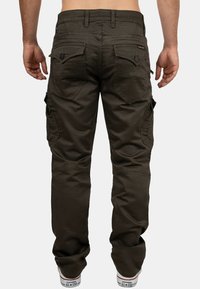 Cargo-Hose in dunklem Olivgrün, mit mehreren Taschen, lockerer Passform und sichtbaren Nähten. Getragen mit weißen Sneakers.