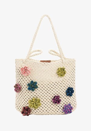 Kreemikavärvi kootud kandekott palmikutega käepidemetega ja mitmevärviliste kangast lilledega, mis on erinevates kohtades kinnitatud.