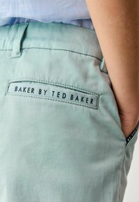 Light green trousers with a smooth texture, featuring a black label on the back pocket that reads "BAKER BY TED BAKER."