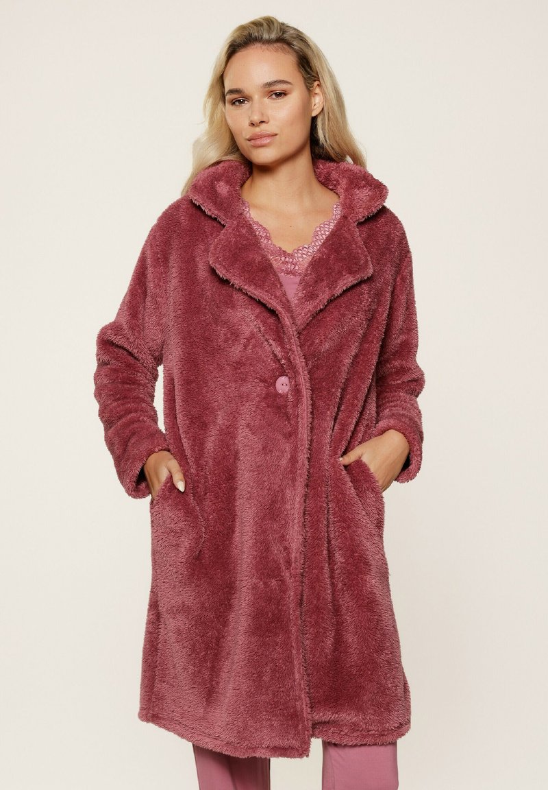 Cappotto in pelliccia sintetica di colore rosa polveroso, con ampio colletto, chiusura con bottoni, maniche lunghe e tasche laterali. Morbida texture su tutta la superficie.