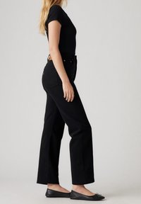 Zwarte high-waisted jeans met rechte pijpen, voorzien van een klassieke snit en achterzakken. Gecombineerd met een zwarte aansluitende top en platte zwarte schoenen.