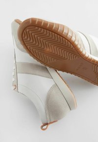 Weiße und beigefarbene Sneakers mit einem strukturierten Obermaterial, Wildlederakzenten, gummierter Sohle und einer Zuglasche an der Ferse. Fischgrätenmuster auf der Sohle.