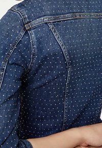 Jeansjacka med rhinestones, mörkblå färg, strukturerad form och klassisk sömnad. Har krage och knappar som detaljer.