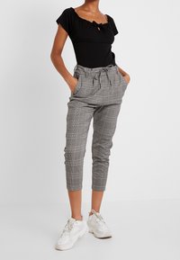 Svart kortärmad bodysuit med nyckelhål; grå rutiga högmidjade byxor med dragsko och uppvikta anklar; vita sneakers.