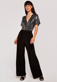 Pantalones de pierna ancha negros con cintura ajustable y top negro brillante de lentejuelas con un escote en V profundo y mangas cortas. Textura suave; diseño elegante.