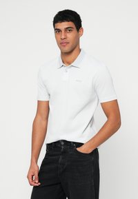 Fehér pólóing klasszikus gallérral, rövid ujjakkal és finom szürke részletekkel. Texturált anyagból készült, a mellrészen 'BOSS' logóval.