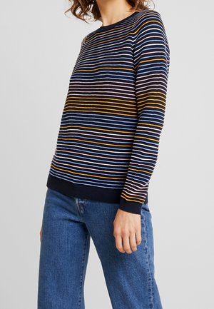 Maglione a maglia blu navy con righe orizzontali in giallo, blu, rosa e bianco. Collo rotondo e polsini a coste, abbinato a jeans blu.