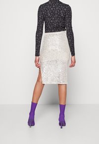 Silver sequin midiklänning med hög slits; kombinerad med en långärmad svart mönstrad topp och lila anklarstövlar.