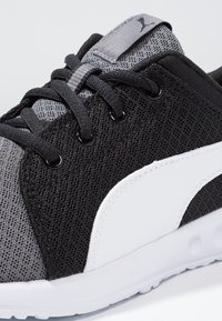 Chaussure de sport noire et grise en matériaux mesh et synthétiques, dotée d'un design à lacets, d'un accent de marque blanc et d'une surface texturée.