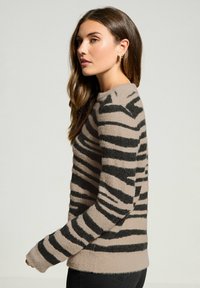 Beige sweater med sorte striber, lavet af blødt, struktureret materiale. Har rund halsudskæring og lange ærmer med ribbede manchetter.