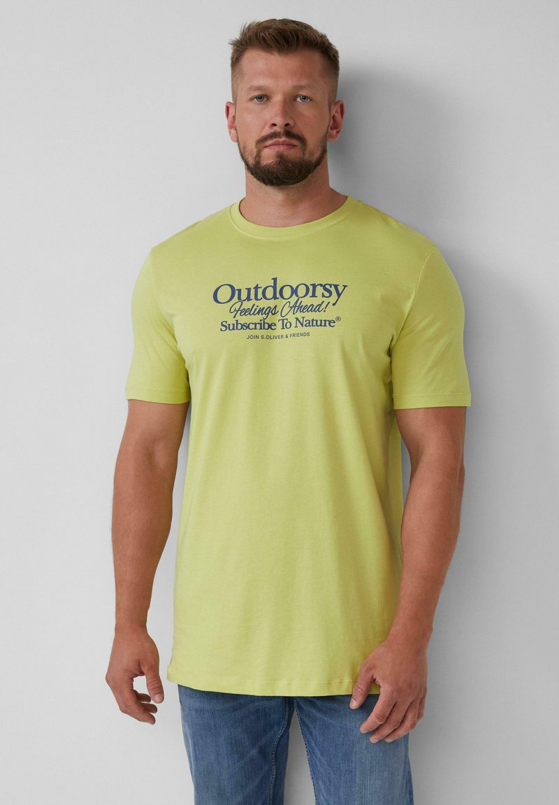 Geel katoenen T-shirt met marineblauwe grafische tekst op de voorkant. Korte mouwen en een relaxte pasvorm, gecombineerd met lichtblauwe jeans.