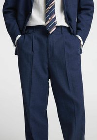 Veste de costume bleu marine et pantalon en tissu texturé, dotés de deux poches avant et d'une cravate rayée bleu marine, blanche et rouge.