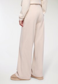 Spodnie w kolorze kremowym z dzianiny waffle, o szerokim kroju i luźnym fasonie, z elastycznym pasem, połączone z beżowymi butami wsuwanymi.