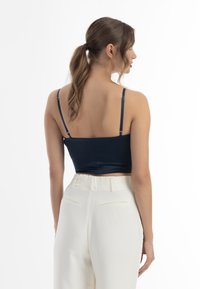 Námořnický crop top s tenkými ramínky, hladkou texturou a přiléhavým střihem. Kombinován s bílými kalhotami s vysokým pasem, které mají zadní kapsy a jemné sklady.