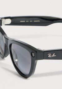 Occhiali da sole neri in plastica con lenti sfumate grigie, caratterizzati da un design quadrato e dal logo Ray-Ban argentato sulla montatura.