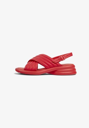 Sandalias rojas con un diseño de tiras cruzadas acolchadas, hebilla ajustable y suela redondeada y estratificada. Textura suave con un acabado brillante.