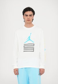 Maglietta bianca a maniche lunghe con logo di basket azzurro chiaro sul davanti e dettagli gialli sulle maniche. Tessuto di cotone morbido, design a girocollo.