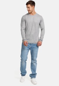 Camiseta gris de manga larga con cuello redondo, combinada con jeans azul claro y zapatillas blancas. La tela parece suave y ligeramente texturizada.